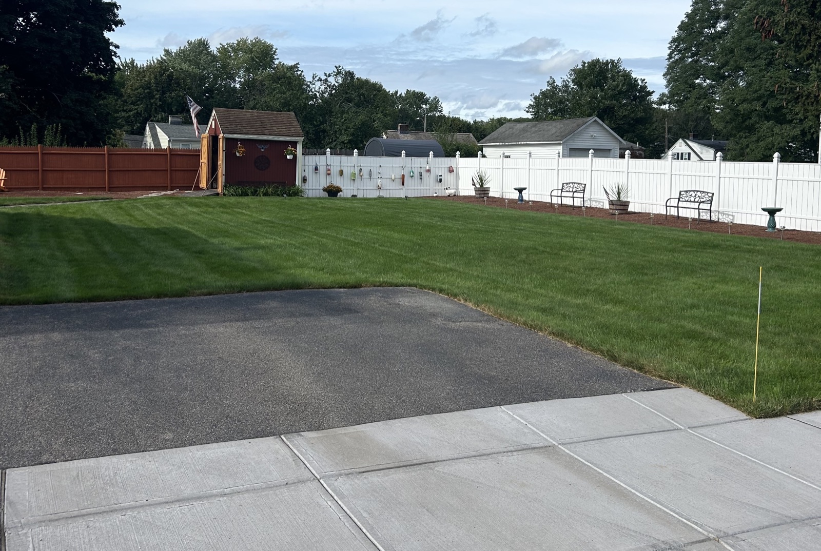 Freshly striped backyard lawn in Norwood, enclosed by a white vinyl fence with a red garden shed and two benches