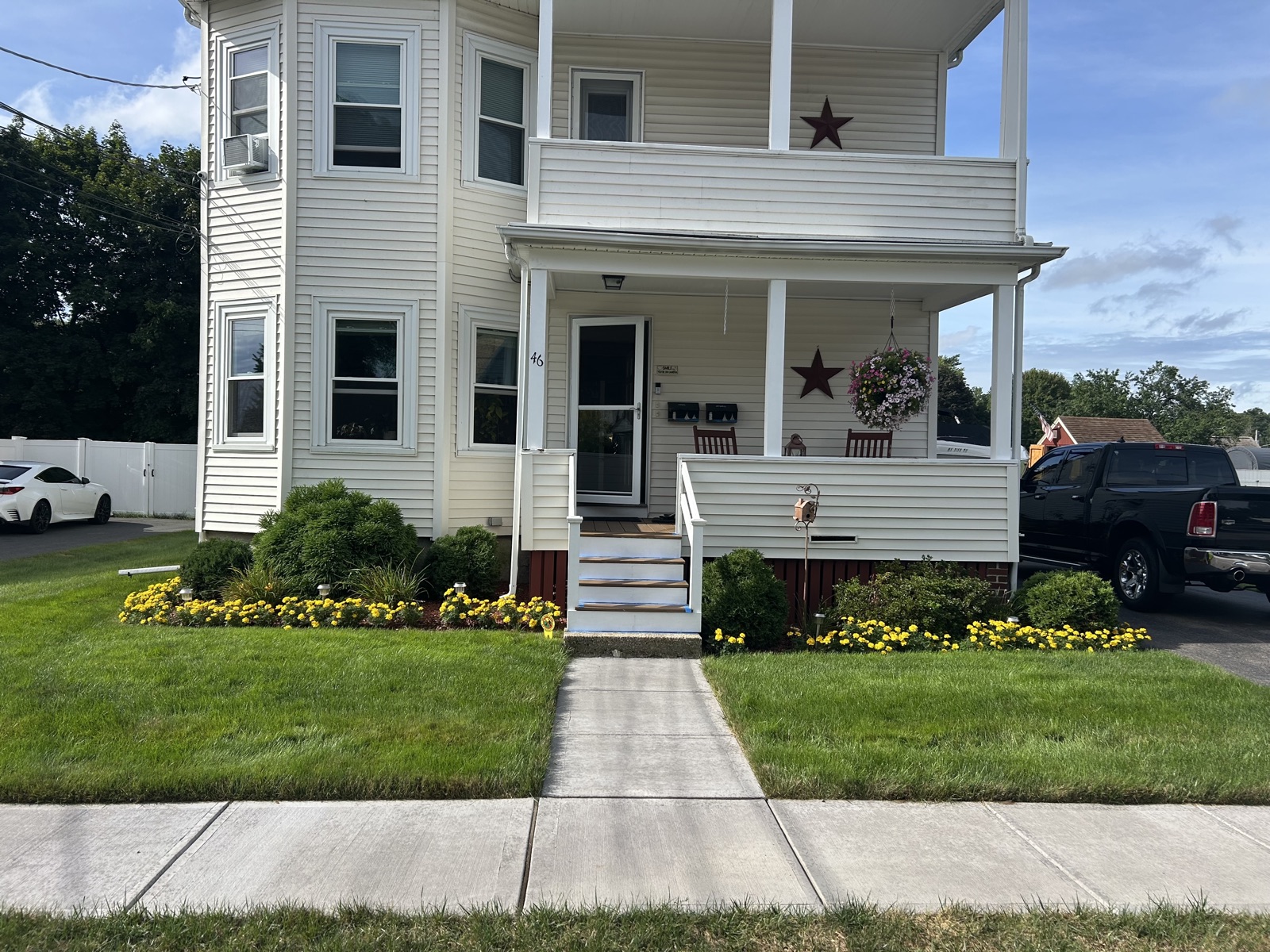 Thick green front lawn on both sides of the walkway at a Norwood two-family home, edged with yellow marigolds